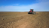 a red tractor plowing a field with a blue sky