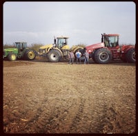 a group of people standing next to tractors in a dirt field