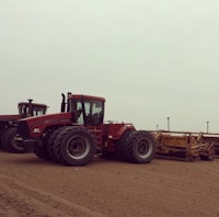 two large red tractors parked on a dirt field