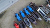 a group of blue dump trucks parked on a dirt road