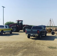 two trucks and a tractor parked in a dirt lot