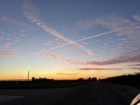 a car driving down a road with a contrail in the sky